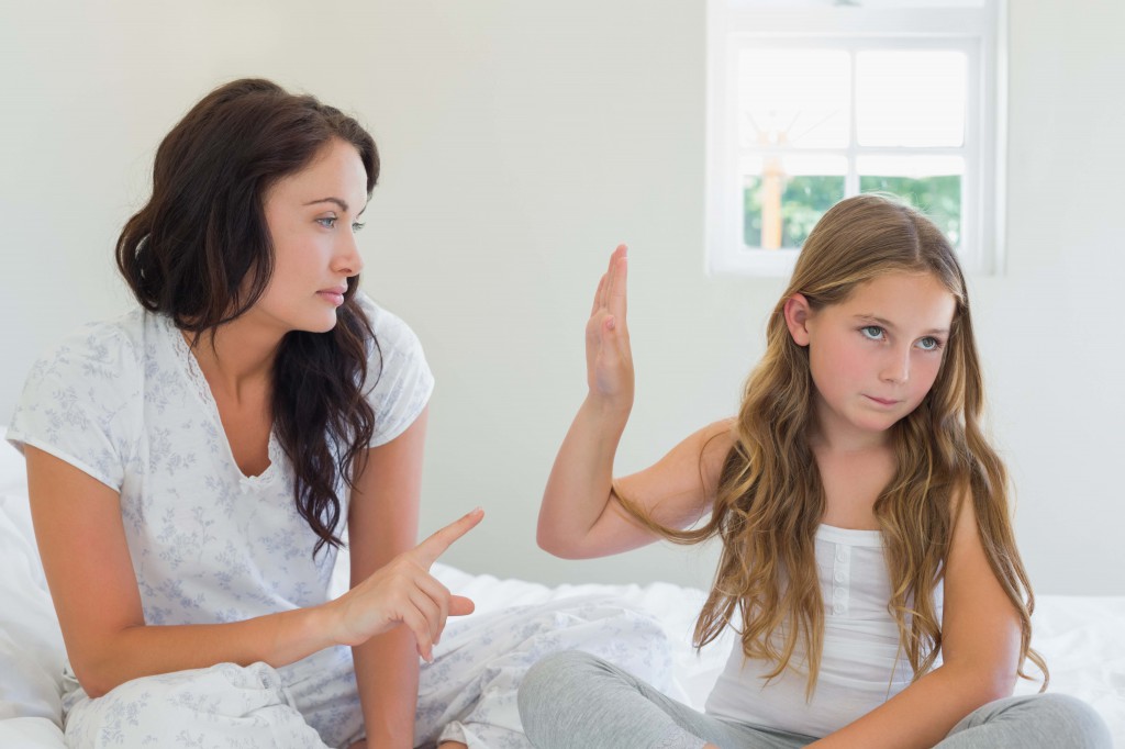 Girl showing stop gesture to angry mother in bed